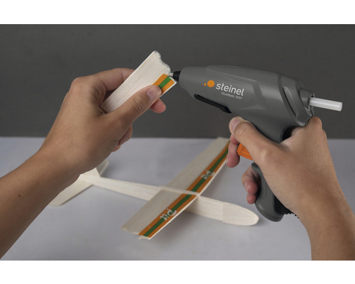 Hand, die mit einer Steinel Heißklebepistole einen Holzgegenstand verklebt