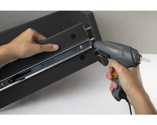 Eine Person befestigt eine Schubladenschiene mit einer Heißklebepistole an einem Möbelstück.