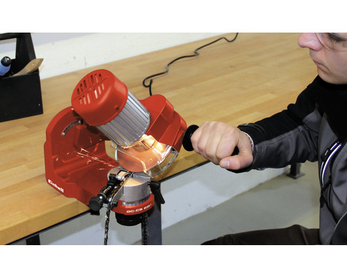 Ein Mann schärft eine Kettensäge mit einem Kettensägenschärfgerät der Marke Einhell.