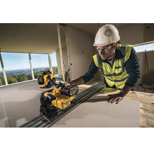 Ein Bauarbeiter mit Helm und Schutzbrille schneidet mit einer DeWalt Gipskartonsäge eine Platte in einem Raum im Rohbau. Ein DeWalt Staubsauger steht im Hintergrund.