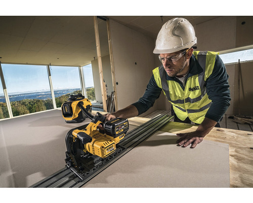 Ein Bauarbeiter mit Helm und Schutzbrille schneidet mit einer DeWalt Gipskartonsäge eine Platte in einem Raum im Rohbau. Ein DeWalt Staubsauger steht im Hintergrund.