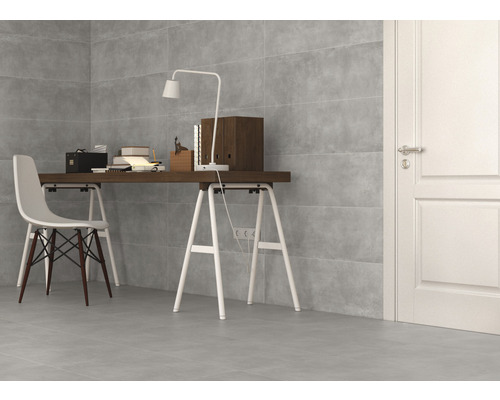 Heller Raum mit grauen Fliesen an Wand und Boden, Schreibtisch mit Lampe, Büchern und Stuhl.