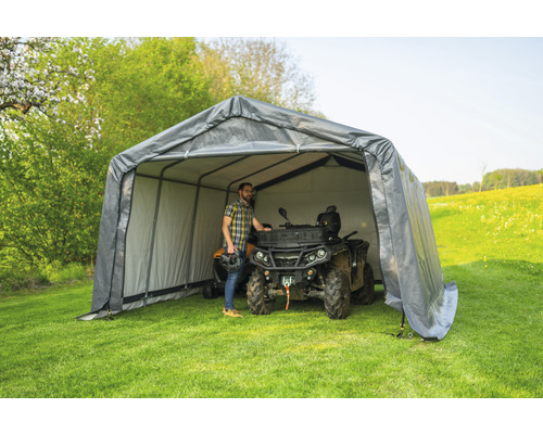 Graue Geräteüberdachung mit einem Mann und einem Quad auf einer Wiese.