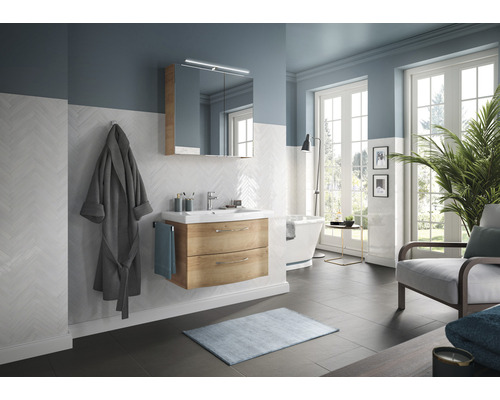 Helles Badezimmer mit Waschtisch, Spiegel, Badewanne und Sessel.