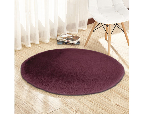 Runder, florartiger Teppich auf Holzboden mit Stuhl und Büchern im Hintergrund.