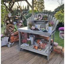 Gartenszene mit Pflanztisch aus Holz und Edelstahloberfläche, dekoriert mit Pflanzen und Gartengeräten.