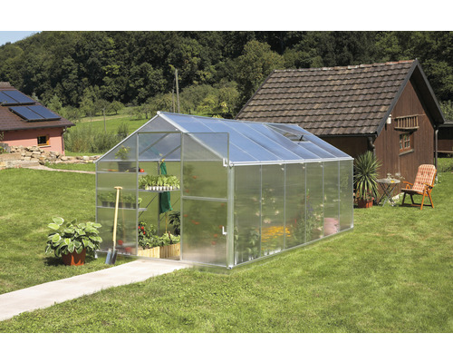 Gewächshaus auf einer Rasenfläche mit Pflanzen darin.