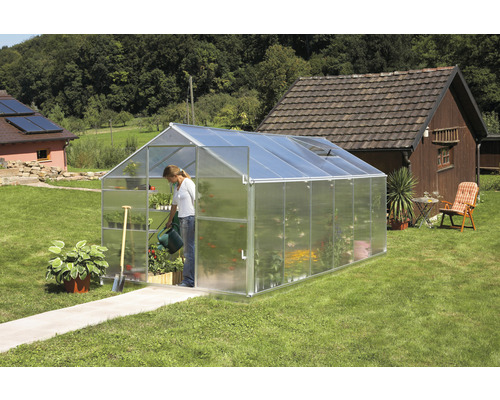 Gewächshaus im Garten mit Frau, die Pflanzen gießt