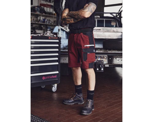 Handwerker in Arbeitsshorts, Sicherheitsschuhen und Werkzeugkasten in einer Werkstatt