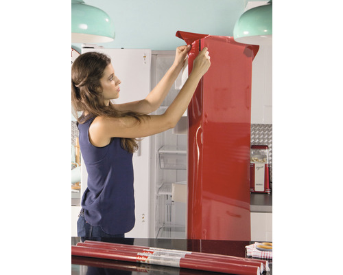 Frau beklebt Kühlschrank mit roter Dekorfolie in Küche.