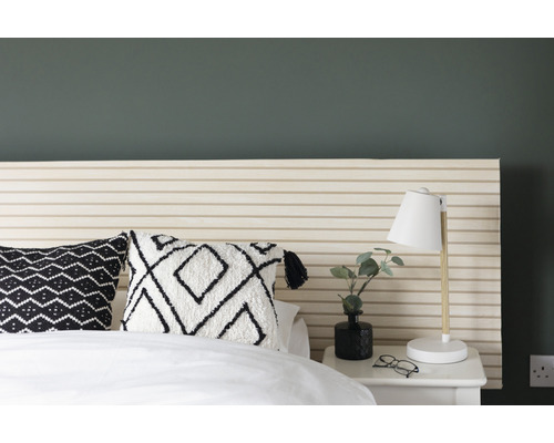 Schlafzimmer mit Bett, gemusterter Bettwäsche, Nachttisch und Lampe