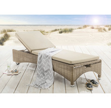 Geflochtene Sonnenliege mit Auflage und Strand im Hintergrund