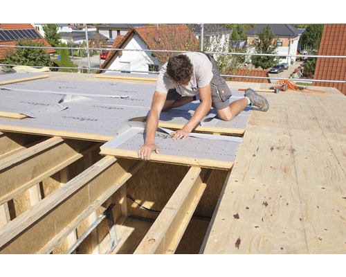 Mann verlegt Dämmplatten auf einem Dachstuhl