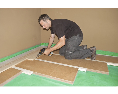 Mann verlegt Trittschalldämmung mit Bohrmaschine in einem Raum.