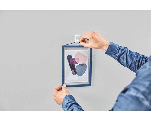 Person hängt gerahmtes Bild mit Klebestreifen an die Wand
