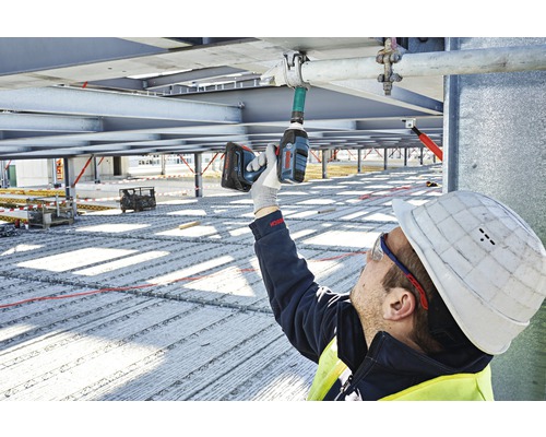 Ein Bauarbeiter montiert mit einem Akku-Bohrschrauber eine Rohrbefestigung an einer Metallstruktur.