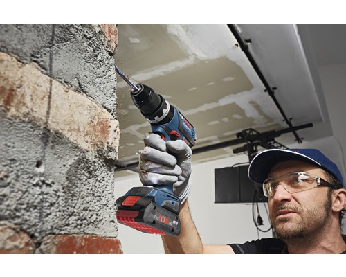 Ein Mann bohrt mit einem Akku-Bohrhammer in eine Ziegelwand.