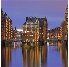 Die Speicherstadt in Hamburg mit beleuchteten Lagerhäusern und Brücken über dem Wasser bei Nacht.