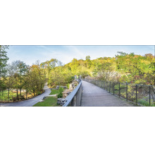 Landschaftsansicht mit Fußgängerbrücke, umgeben von Bäumen und Grünflächen.