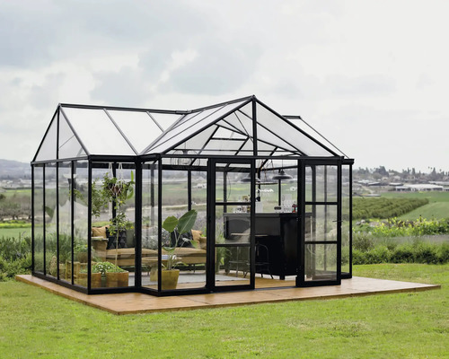 Gewächshaus Palram – Canopia Triomphe Polycarbonat 2 mm 454 x 380 cm schwarz Geräumiges Gewächshaus mit Sitzbereich und Bar auf einer Holzterrasse in einem Garten.