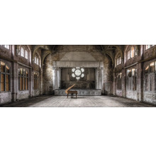 Großer Saal mit Bühne, Klavier und großen Fenstern in einem renovierungsbedürftigen Gebäude.