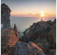 Landschaft mit Felsen, Meer und Leuchtturm im Abendrot.