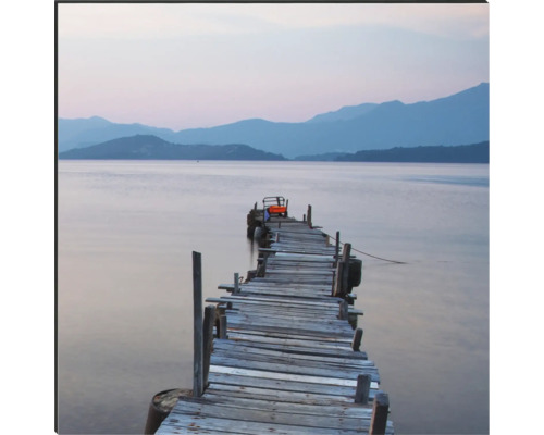 Ein Holzsteg führt in einen See vor einer Hügellandschaft.