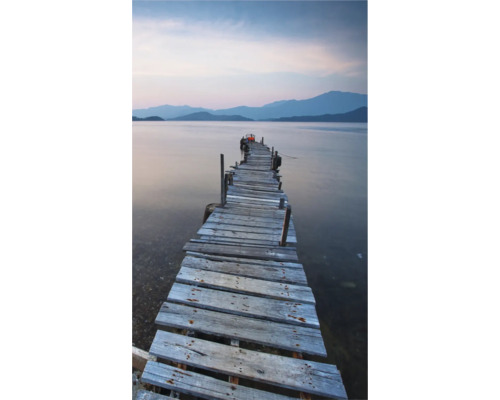 Ein Holzsteg führt ins ruhige Wasser mit Bergen im Hintergrund.