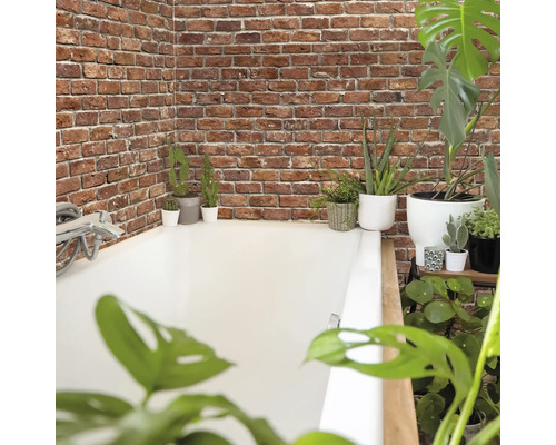 Badezimmer mit Badewanne, Ziegelwand und verschiedenen Pflanzen.