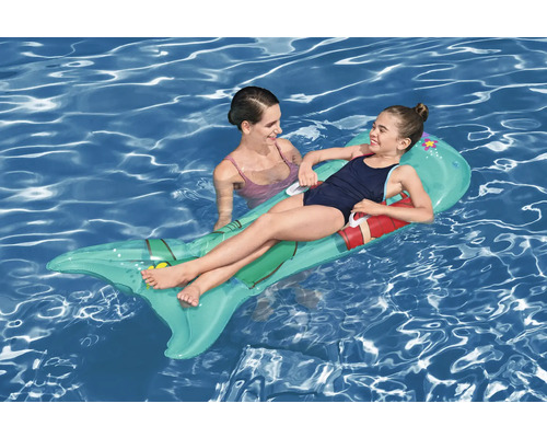 Mädchen liegt auf einer aufblasbaren Fisch Luftmatratze im Wasser, daneben steht eine Frau.