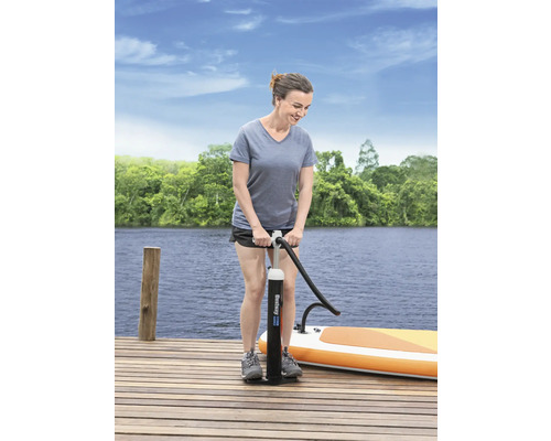 Frau pumpt ein Stand-Up-Paddleboard mit einer Handpumpe auf einem Holzsteg auf