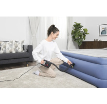 Frau pumpt Luftmatratze mit einer elektrischen Pumpe in einem hellen Wohnzimmer auf