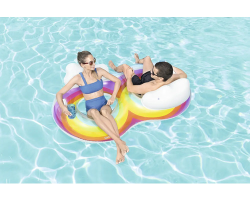 Zwei Personen entspannen auf einer aufblasbaren Regenbogen-Poolinsel im Wasser.