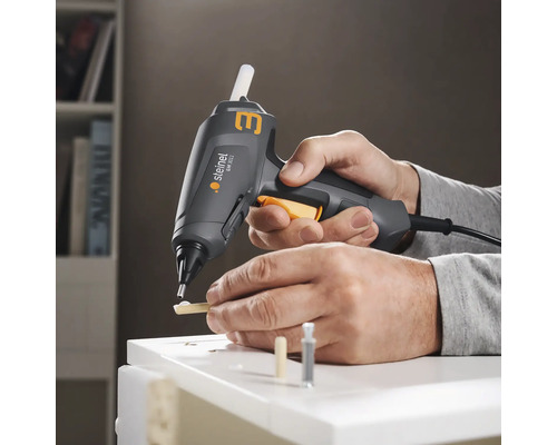 Person verwendet Heißklebepistole von Steinel zum Verkleben von Holzstücken auf einer weißen Oberfläche