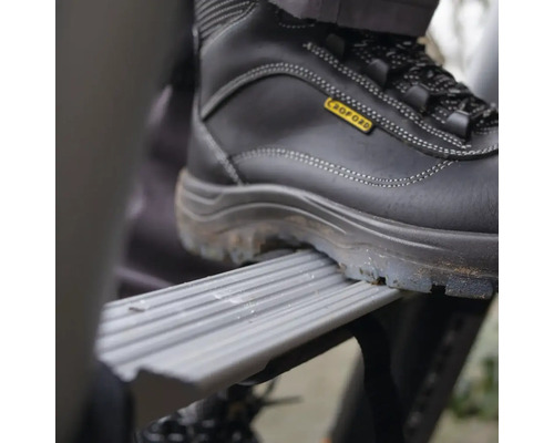 Ein Fuß in einem Sicherheitsschuh auf einer Trittstufe einer Leiter.