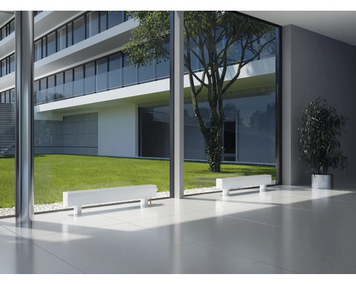 Heller Raum mit weißen Heizkörpern vor einer großen Fensterfront mit Blick auf ein modernes Gebäude und einen Garten.