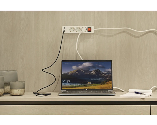 Laptop, Smartphone und Steckdosenleiste auf einem Schreibtisch.