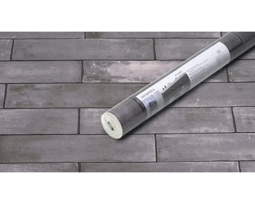 Verpackte Tapetenrolle vor einer Wand mit Ziegelmuster