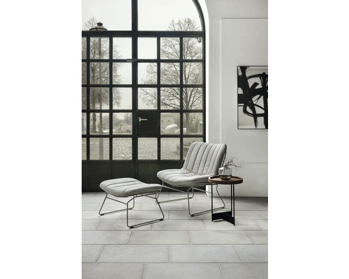 Modernes Wohnzimmer mit Sessel, Fußhocker und Beistelltisch vor einem Sprossenfenster.