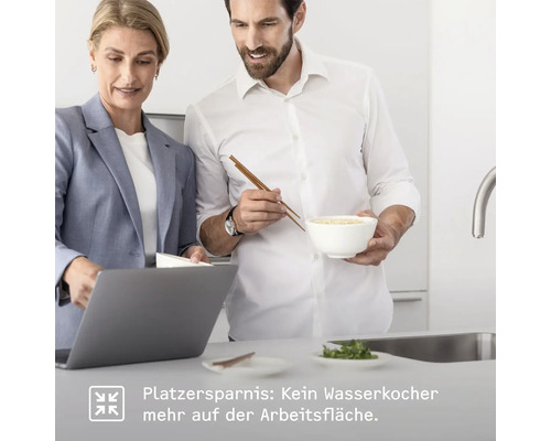 Zwei Personen in einer Küche: Eine Frau arbeitet am Laptop, während ein Mann mit Stäbchen eine Schale hält. Fokus auf Platzersparnis ohne Wasserkocher auf der Arbeitsfläche.