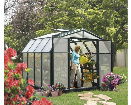 Gewächshaus mit Pflanzen und einer Frau, die mit einer Gießkanne gießt, im Garten.