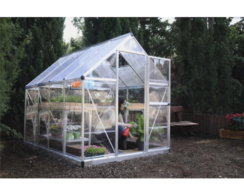 Gewächshaus mit Regalen und einer Person, die eine Pflanze gießt, im Garten