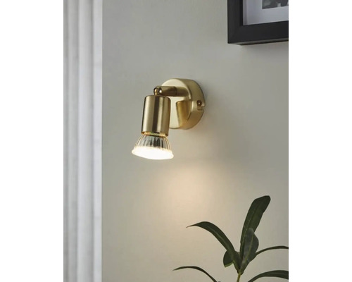 Goldfarbene Wandleuchte mit klarem Glasdiffusor an einer Wand montiert.