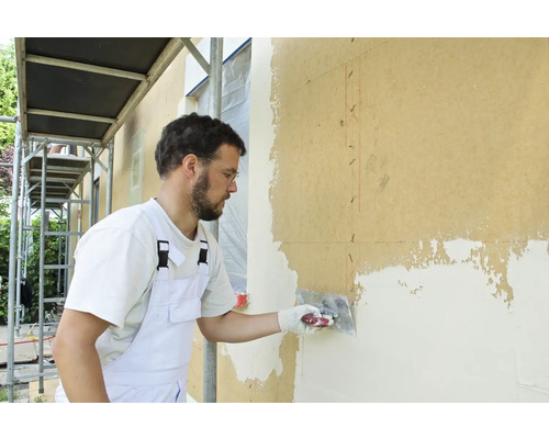 Ein Mann verputzt eine Hauswand mit einem Spachtel.
