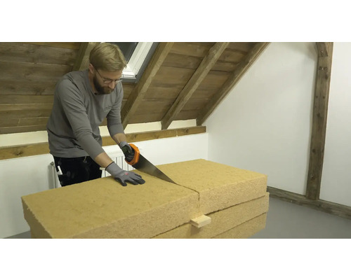 Ein Mann sägt eine Dämmplatte in einem Dachgeschoss.