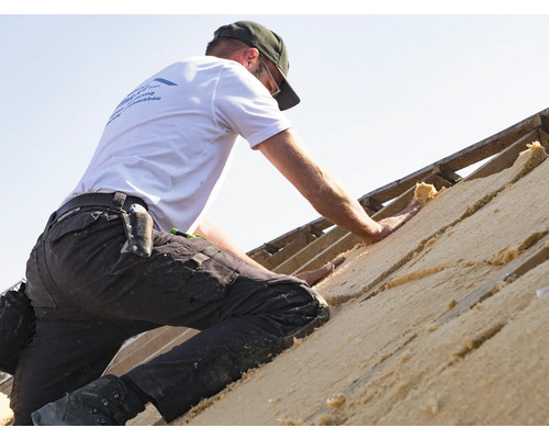 Ein Mann dämmt ein Dach mit Dämmmaterial.