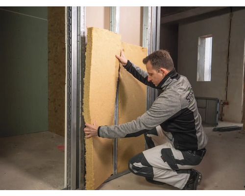 Ein Mann montiert Dämmmaterial in einem Trockenbaurahmen.