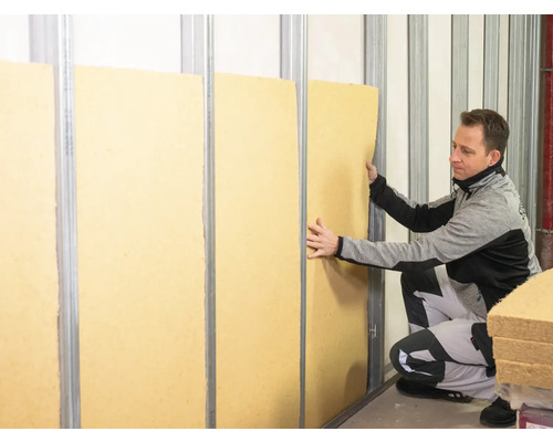 Ein Mann bringt Dämmplatten zwischen Metallständerprofile an.