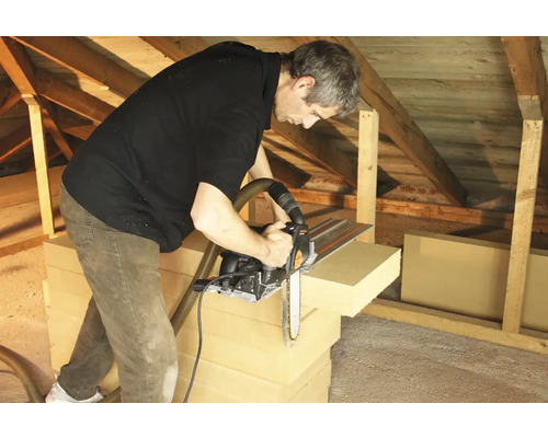 Mann schneidet Dämmplatten mit einer Kettensäge im Dachgeschoss zu.