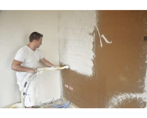 Mann trägt Putz mit einer Putzmaschine auf eine Wand auf.